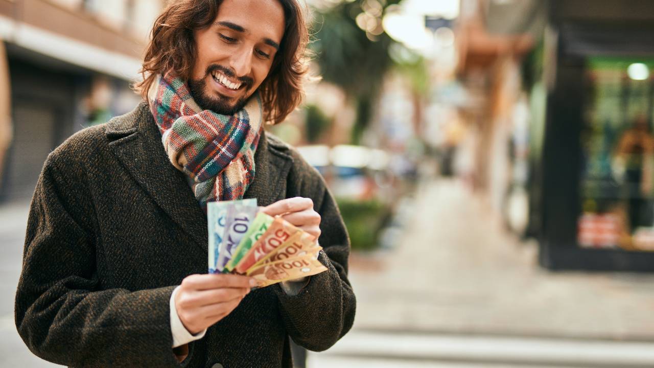 Young hispanic man smiling happy counting canadian dollars at the city